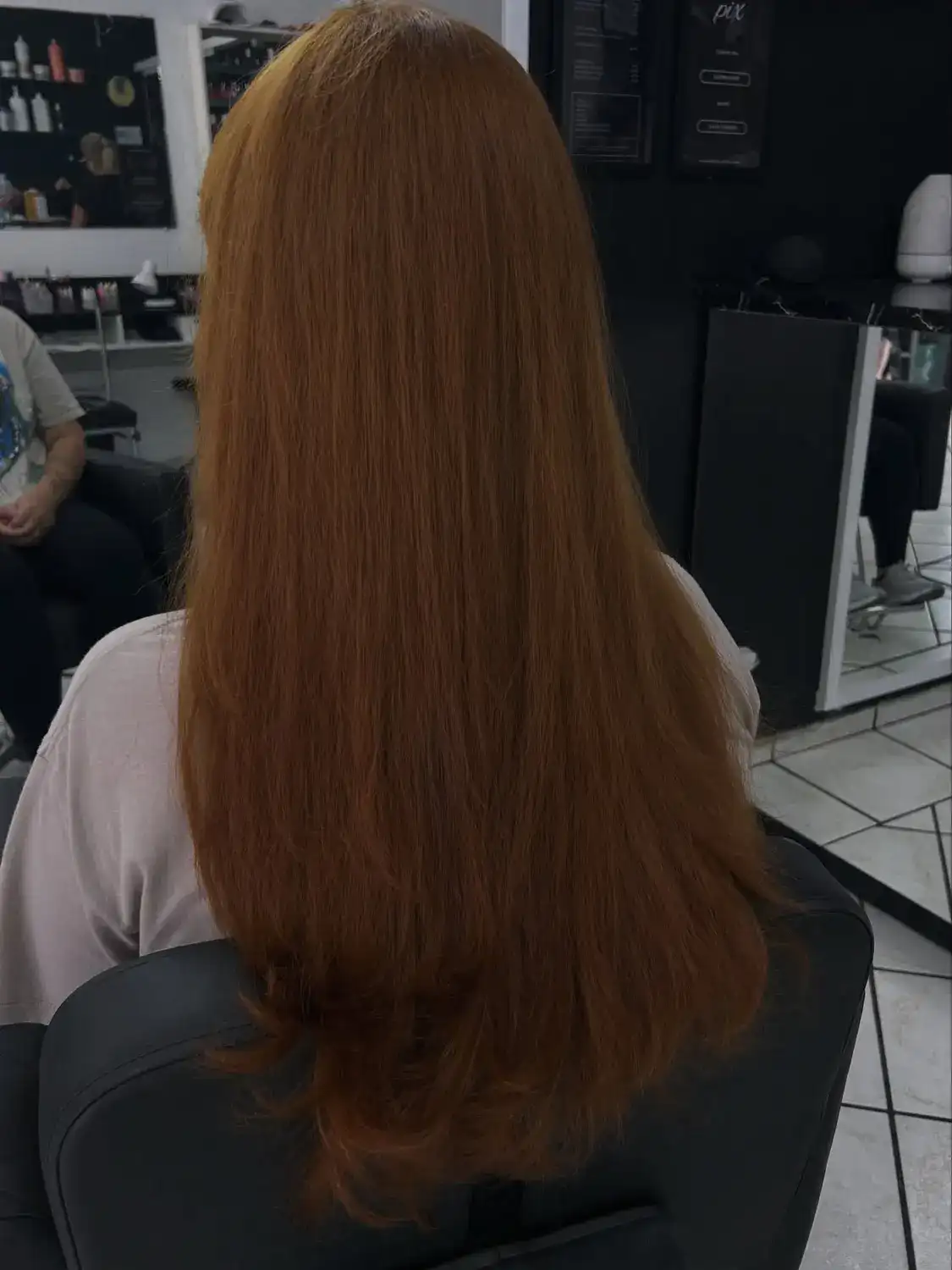 Cabelo ruivo longo com corte repicado e escova, de costas no salão